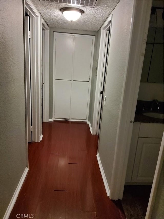 corridor with a textured ceiling, dark hardwood / wood-style flooring, and sink