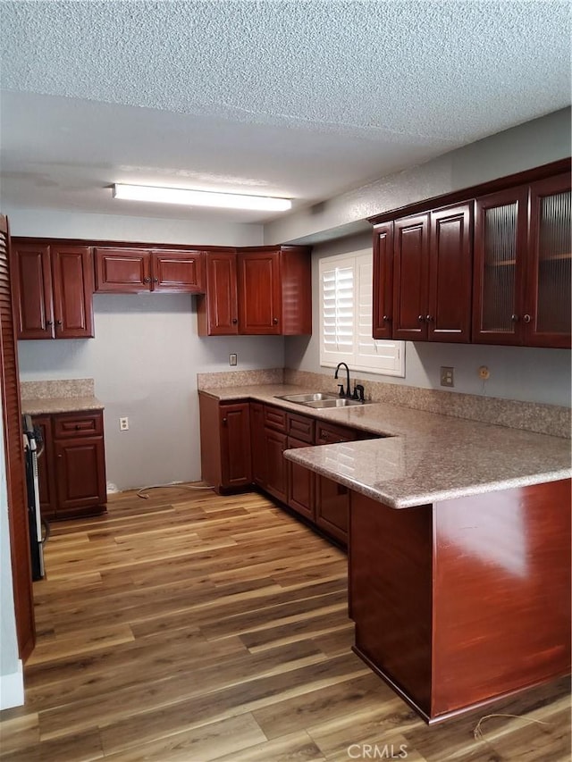 kitchen featuring a textured ceiling, kitchen peninsula, wood-type flooring, and sink