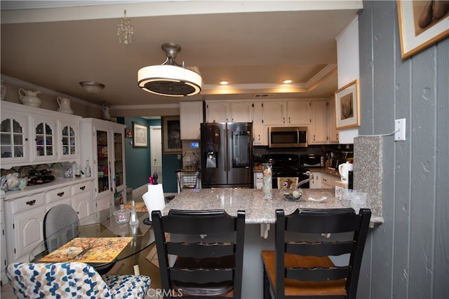 kitchen with ornamental molding, kitchen peninsula, white cabinetry, a tray ceiling, and stainless steel appliances