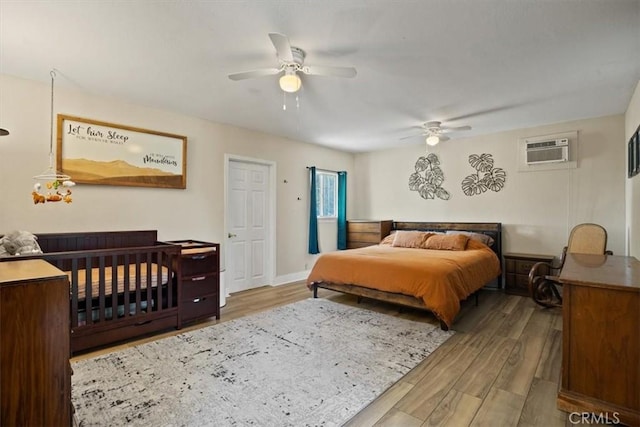 bedroom with ceiling fan, light wood-type flooring, and a wall mounted AC