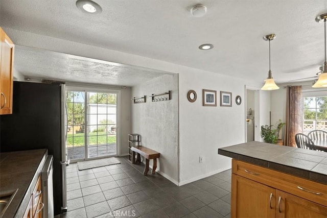 kitchen featuring a textured ceiling, a wealth of natural light, dark tile patterned flooring, and decorative light fixtures