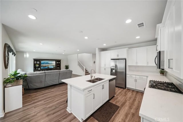 kitchen with a kitchen island with sink, white cabinets, sink, light hardwood / wood-style floors, and stainless steel appliances