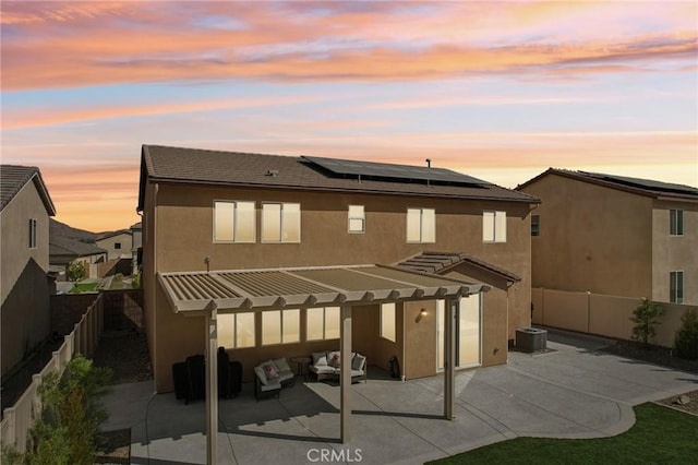 back house at dusk with outdoor lounge area, solar panels, central AC unit, and a patio area