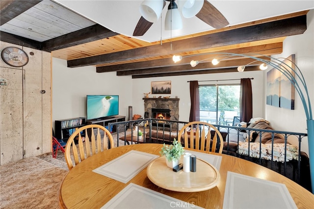 dining area featuring ceiling fan, a fireplace, beam ceiling, and wood ceiling