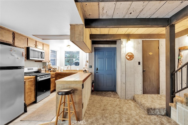 kitchen with beamed ceiling, appliances with stainless steel finishes, light tile patterned flooring, and a breakfast bar area