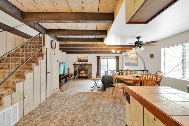 dining space with a fireplace, beam ceiling, light colored carpet, and plenty of natural light