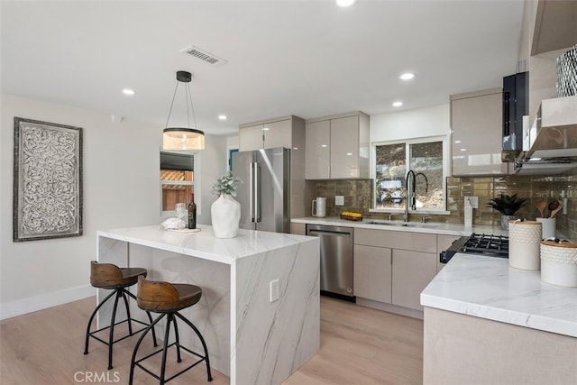 kitchen with decorative backsplash, appliances with stainless steel finishes, sink, light hardwood / wood-style floors, and hanging light fixtures