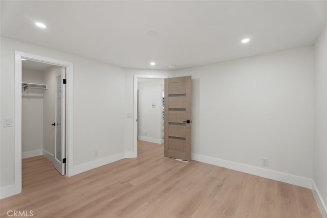 unfurnished bedroom with a walk in closet, light wood-type flooring, and a closet