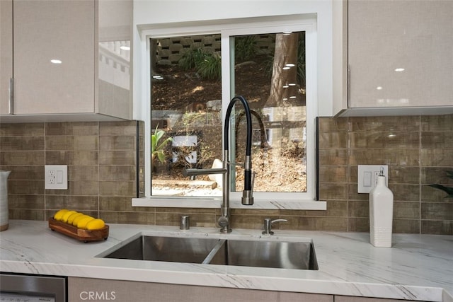 kitchen with tasteful backsplash, light stone counters, and sink