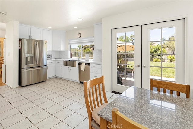 kitchen with appliances with stainless steel finishes, light tile patterned flooring, french doors, white cabinets, and decorative backsplash