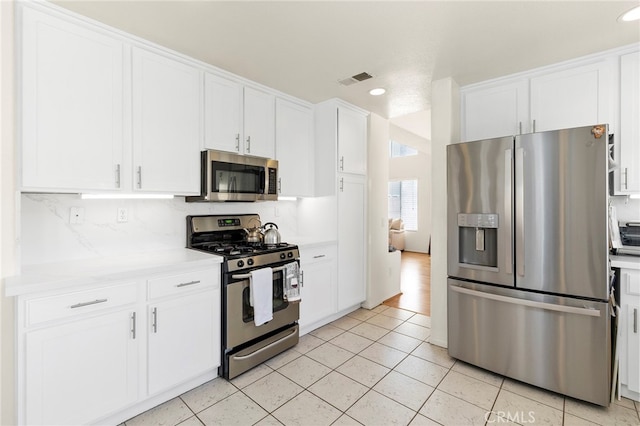 kitchen featuring tasteful backsplash, appliances with stainless steel finishes, light tile patterned flooring, and white cabinets