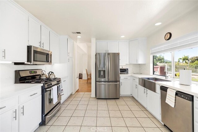 kitchen with sink, appliances with stainless steel finishes, white cabinetry, and light tile patterned flooring