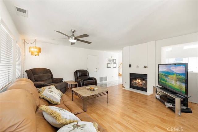 living room featuring ceiling fan with notable chandelier and light wood-type flooring