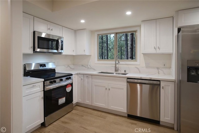 kitchen featuring light wood finished floors, appliances with stainless steel finishes, a sink, and white cabinets