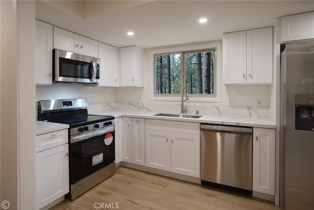 kitchen with light stone counters, appliances with stainless steel finishes, white cabinets, a sink, and light wood-type flooring