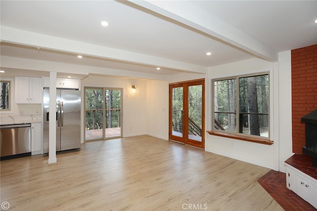 unfurnished living room with beam ceiling, plenty of natural light, light wood finished floors, and french doors