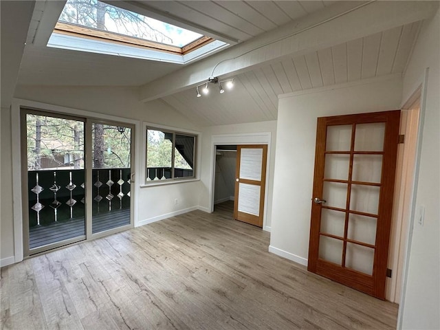 spare room featuring vaulted ceiling with skylight, baseboards, and wood finished floors