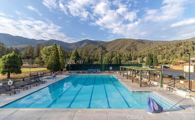 pool featuring a mountain view, a patio, a forest view, and fence