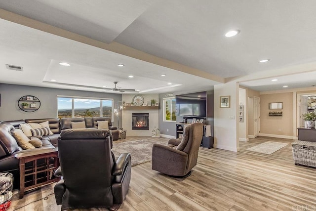 living room with a raised ceiling, ceiling fan, and light hardwood / wood-style floors