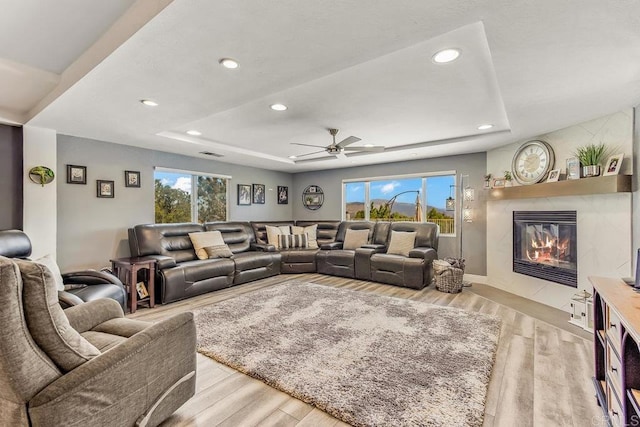 living room with a fireplace, a tray ceiling, light hardwood / wood-style flooring, and ceiling fan