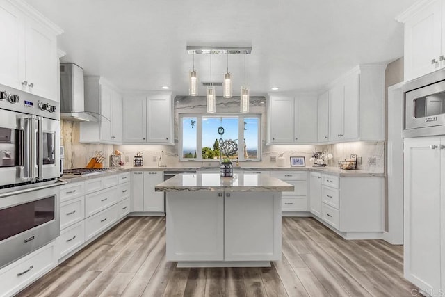 kitchen featuring wall chimney range hood, a kitchen island, appliances with stainless steel finishes, light hardwood / wood-style floors, and white cabinetry