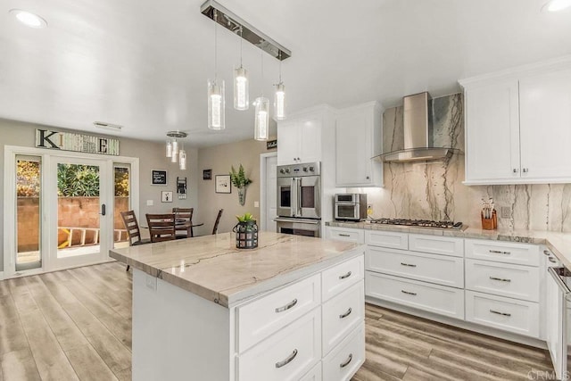 kitchen featuring wall chimney exhaust hood, light stone countertops, light wood-type flooring, a kitchen island, and white cabinetry