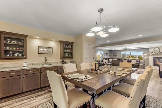 dining area featuring ceiling fan with notable chandelier, light wood-type flooring, and sink