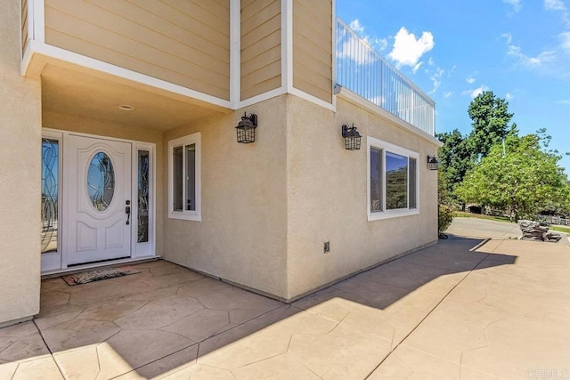 view of exterior entry featuring a patio area and a balcony