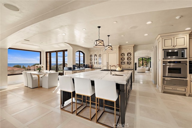 kitchen with cream cabinets, pendant lighting, appliances with stainless steel finishes, and a kitchen island with sink