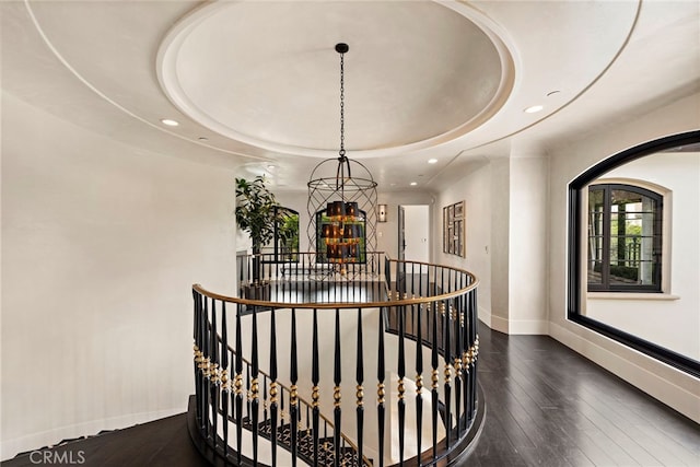 staircase featuring wood-type flooring, a tray ceiling, and a notable chandelier