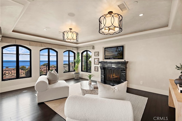 living room featuring a raised ceiling, dark hardwood / wood-style floors, a water view, and a wealth of natural light