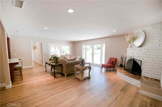 living room featuring french doors, light wood-type flooring, and a brick fireplace