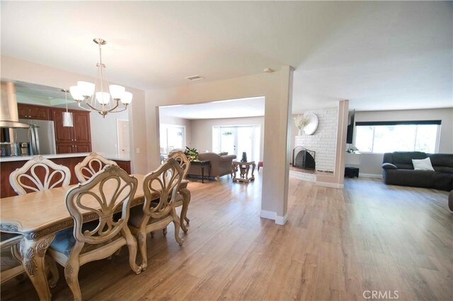 dining area with light hardwood / wood-style flooring, a chandelier, and a brick fireplace