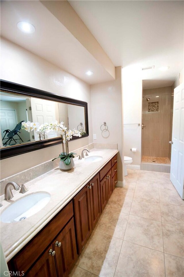 bathroom with tile patterned flooring, a tile shower, vanity, and toilet