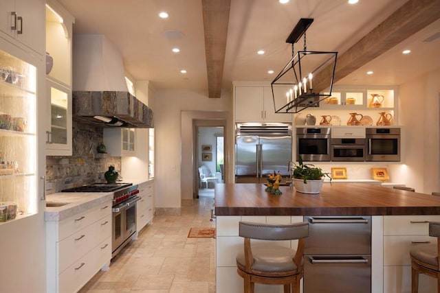 kitchen with premium appliances, wall chimney exhaust hood, white cabinetry, butcher block counters, and beam ceiling