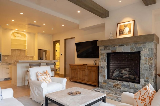 living room with beam ceiling, a stone fireplace, and light hardwood / wood-style floors