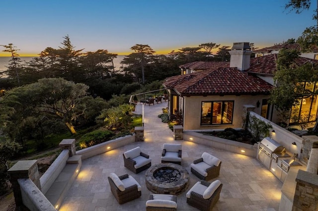 back house at dusk featuring an outdoor fire pit, a patio, and an outdoor kitchen