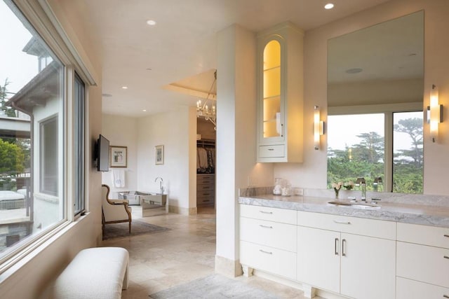 kitchen featuring light stone countertops, white cabinets, an inviting chandelier, and sink