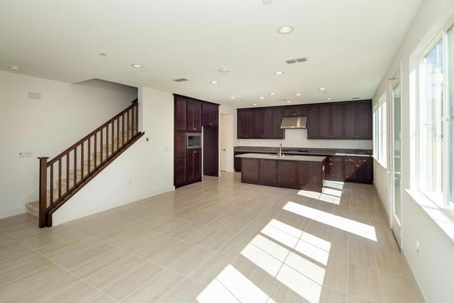 kitchen featuring light tile patterned floors, sink, dark brown cabinets, and an island with sink