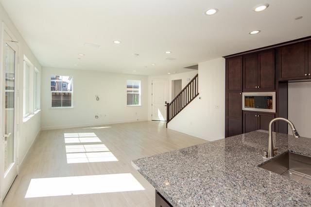 kitchen featuring white microwave, dark brown cabinets, light stone countertops, light hardwood / wood-style flooring, and sink