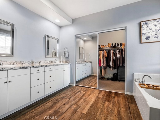 bathroom featuring a relaxing tiled tub, hardwood / wood-style flooring, and vanity