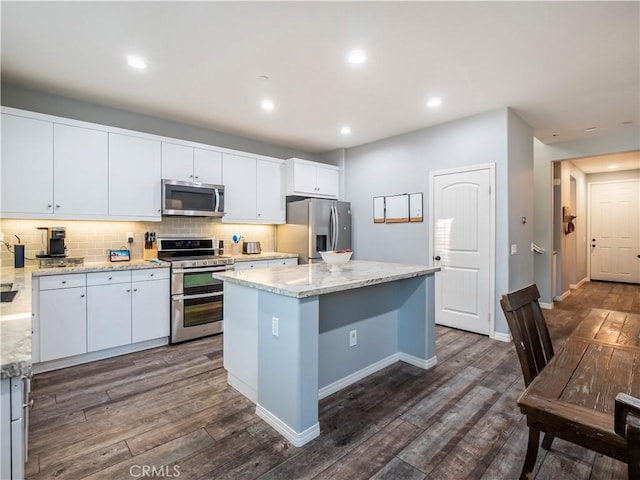 kitchen with light stone countertops, appliances with stainless steel finishes, a kitchen island, white cabinetry, and dark hardwood / wood-style floors