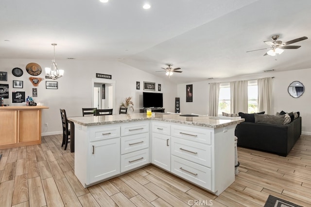 kitchen featuring light wood-type flooring, a center island, white cabinets, vaulted ceiling, and decorative light fixtures