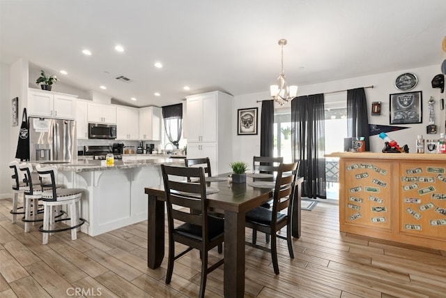 dining area featuring vaulted ceiling, a notable chandelier, and light hardwood / wood-style floors