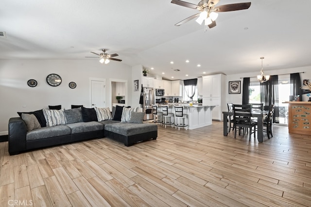 living room featuring ceiling fan with notable chandelier, vaulted ceiling, and light hardwood / wood-style flooring