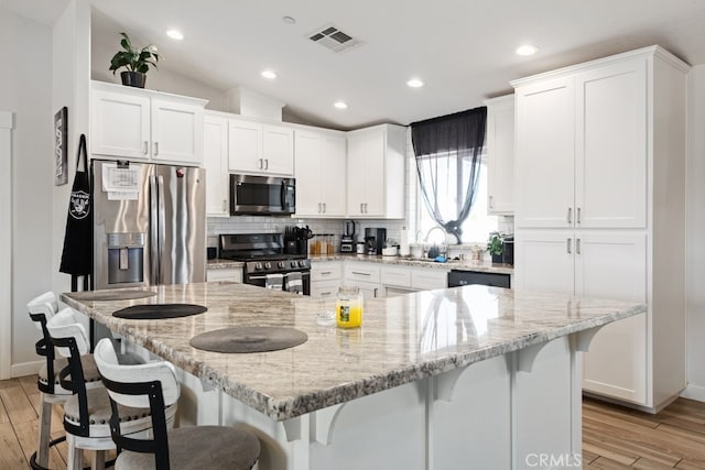 kitchen with appliances with stainless steel finishes, light wood-type flooring, a kitchen island, and white cabinets