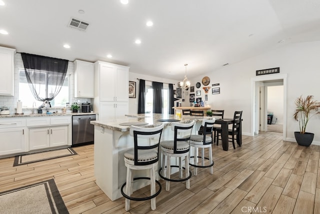 kitchen featuring a center island, plenty of natural light, white cabinets, vaulted ceiling, and stainless steel dishwasher