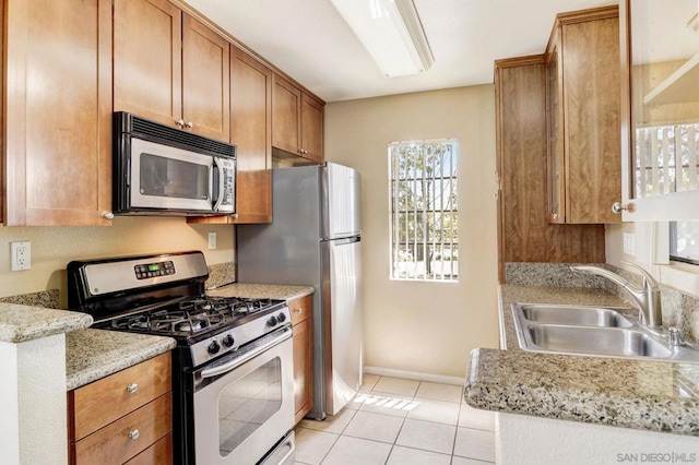 kitchen with light stone counters, appliances with stainless steel finishes, light tile patterned flooring, and sink