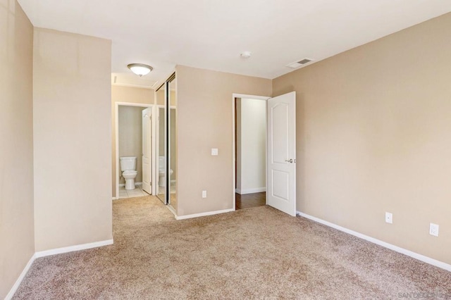 unfurnished bedroom featuring light colored carpet, a closet, and ensuite bathroom