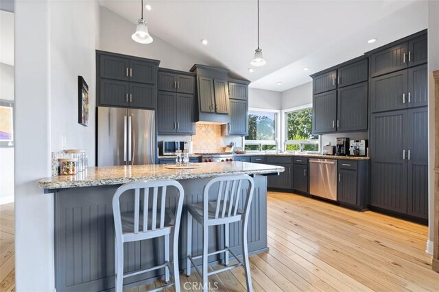 kitchen with tasteful backsplash, hanging light fixtures, light hardwood / wood-style flooring, kitchen peninsula, and stainless steel appliances